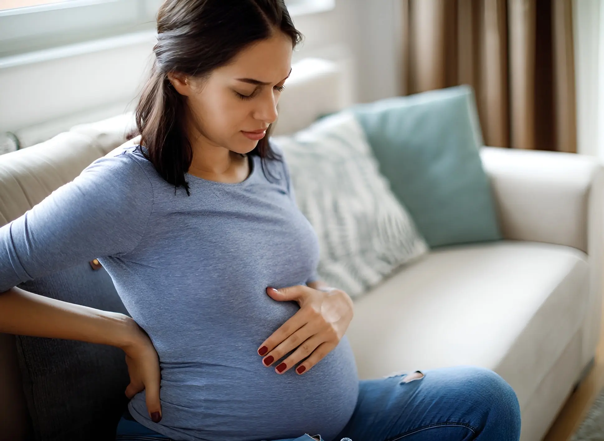 Pregnant woman sitting, holding her belly thoughtfully