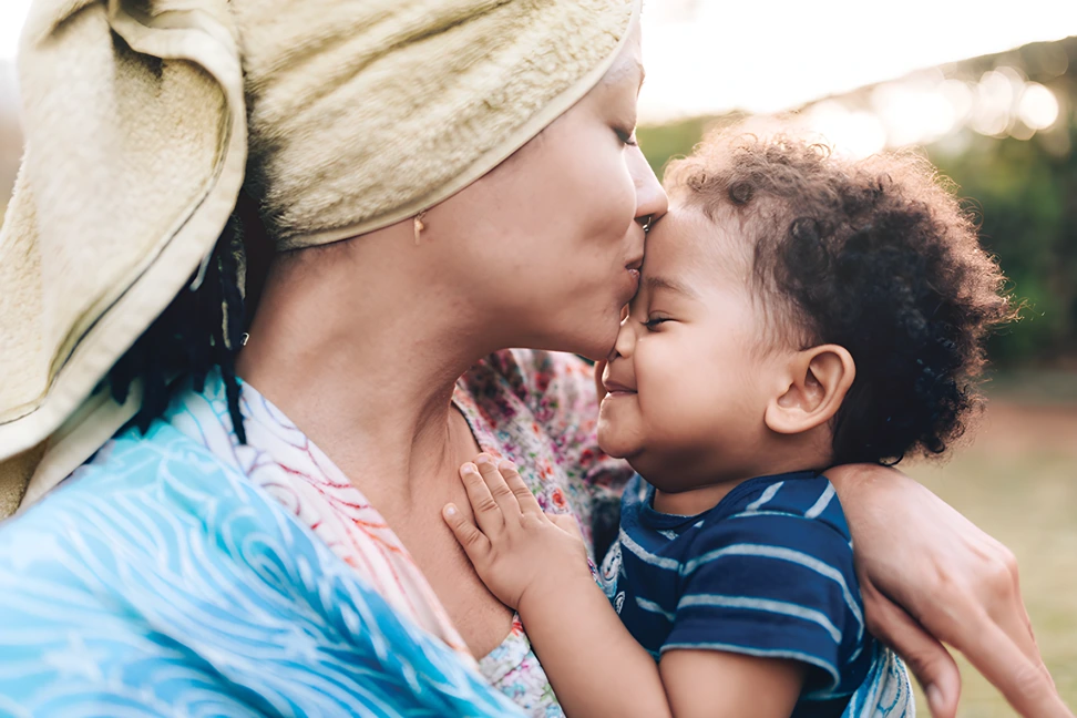 Mother kissing smiling toddler outdoors