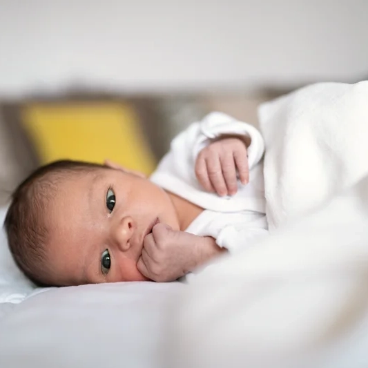Baby lying on bed, looking alert and calm