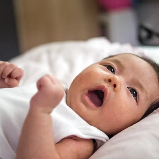 Baby lying down, clenching hands, looking up