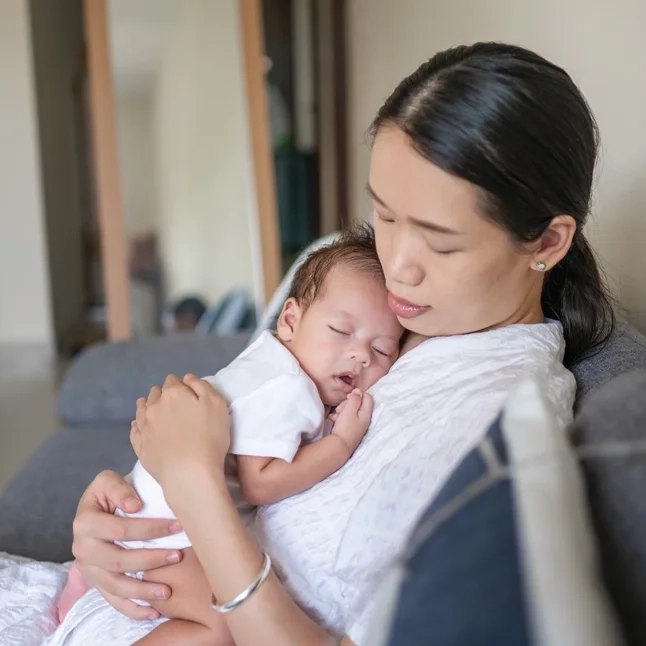 Mother holding sleeping baby on couch