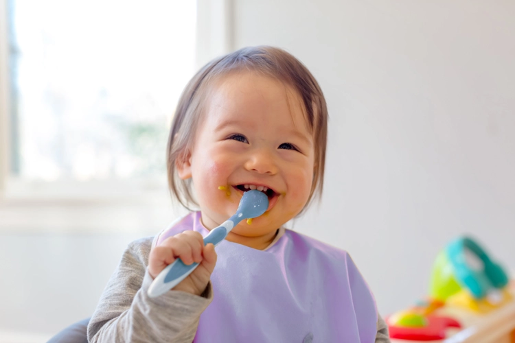 Baby smiling while eating with spoon