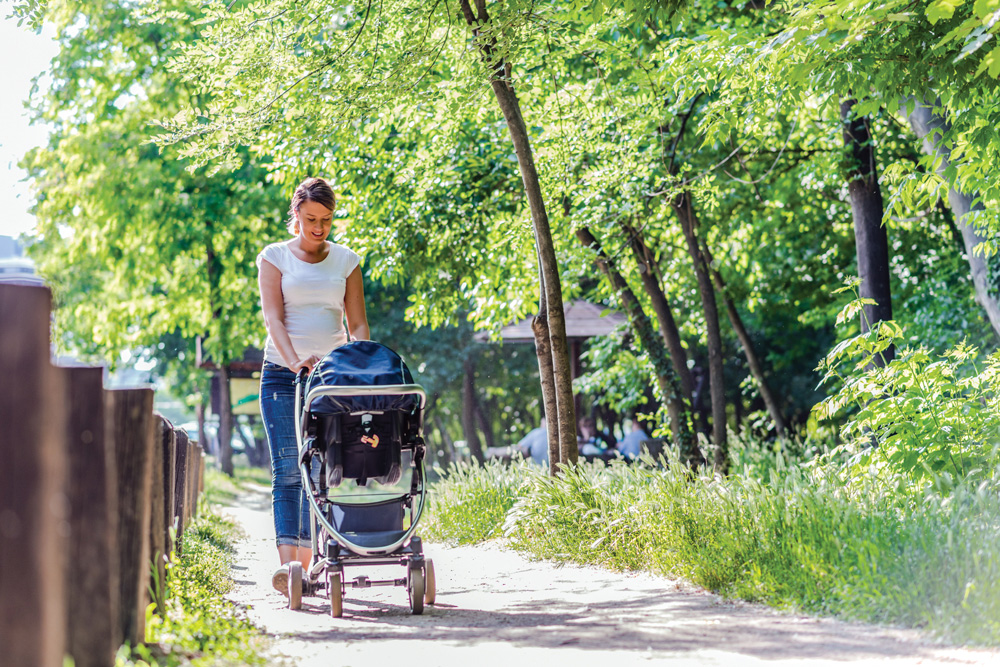 Mother pushing stroller along a sunny path