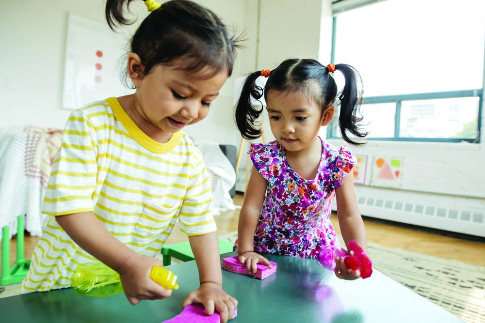 Two young girls cleaning a table together