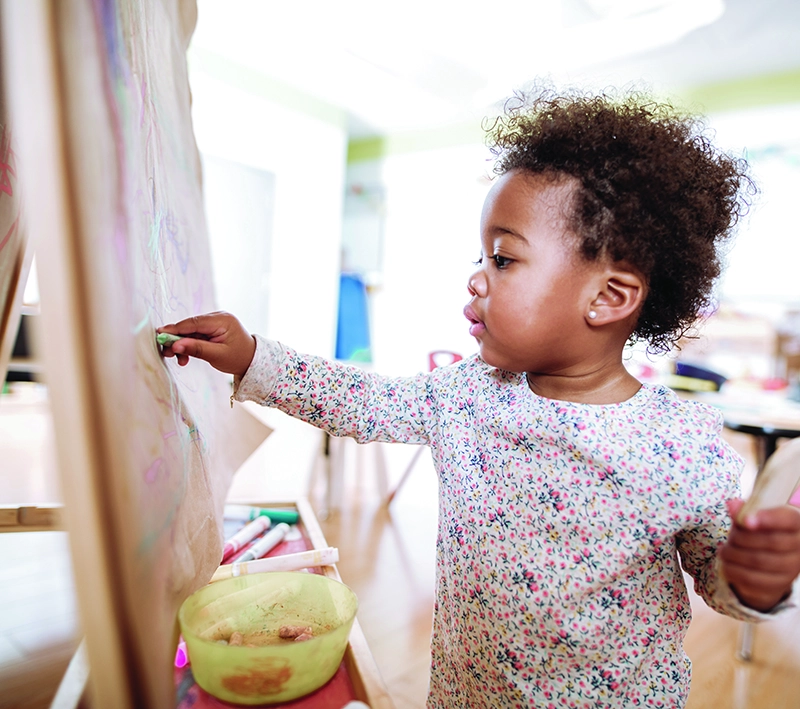 Toddler drawing on easel with colorful chalk