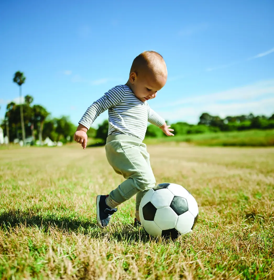 Toddler playing soccer on grass field