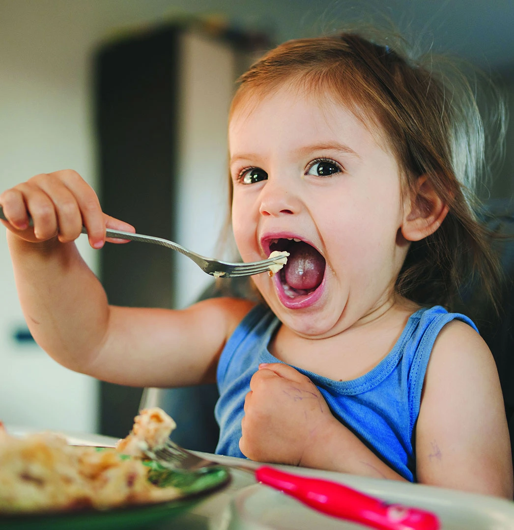 Toddler eagerly eating with a fork