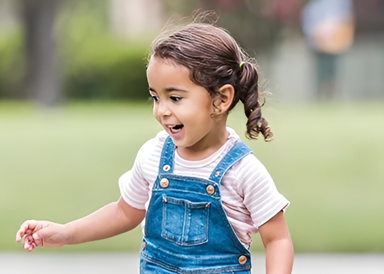 Young girl joyfully playing outside in overalls