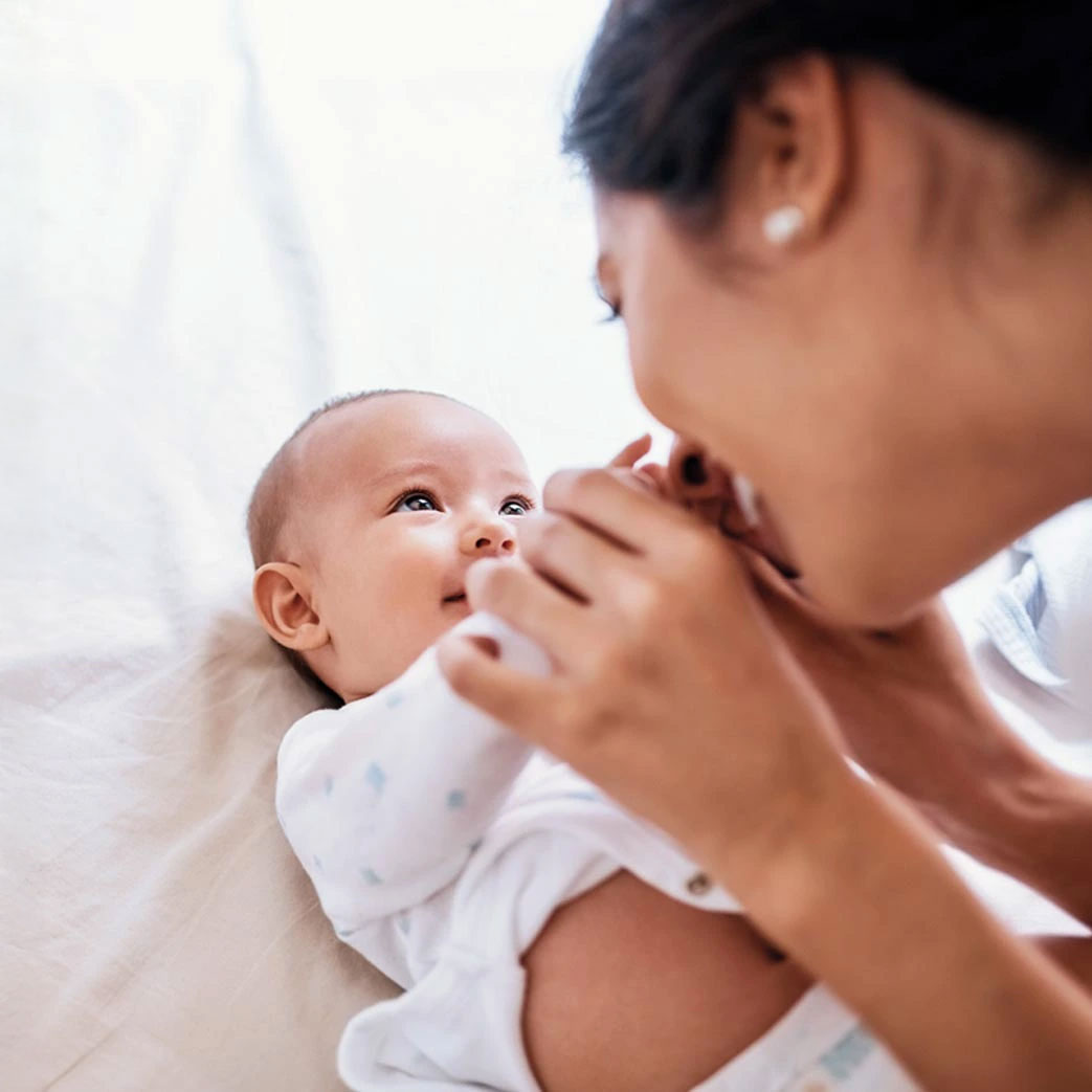 Mother cuddling smiling baby on white bed