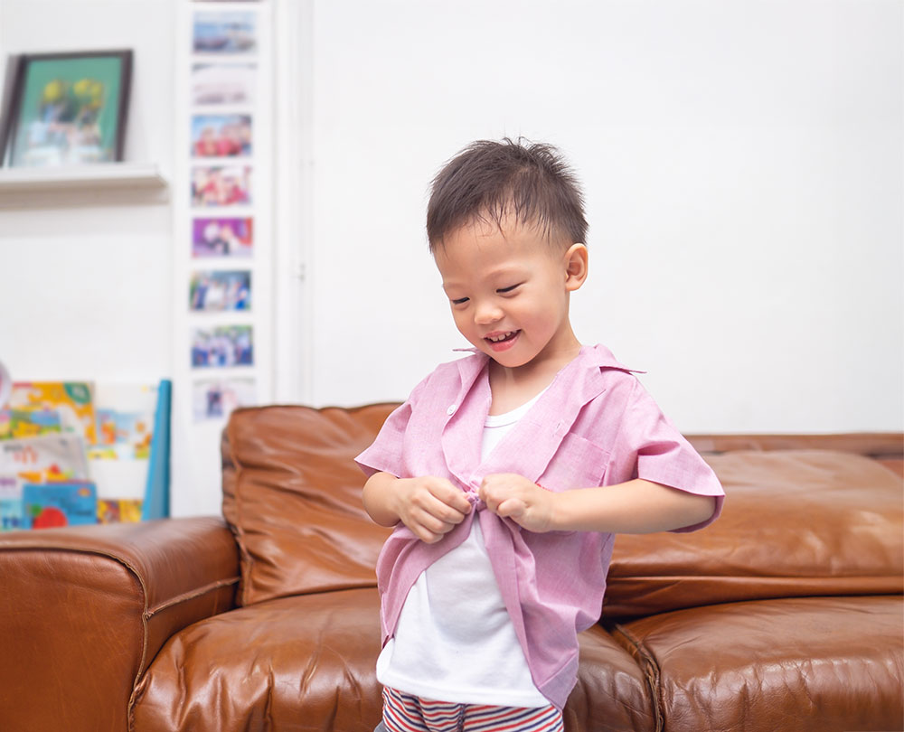 Young boy unbuttoning pink shirt, smiling