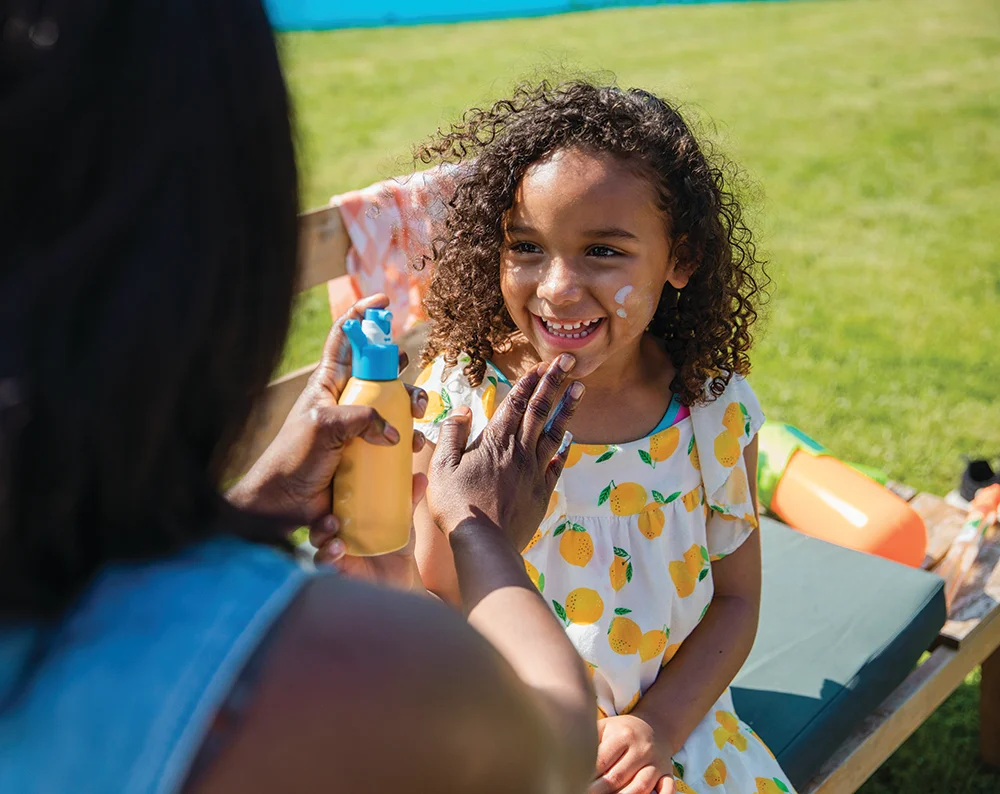 Mom applying sunscreen to smiling daughter outdoors